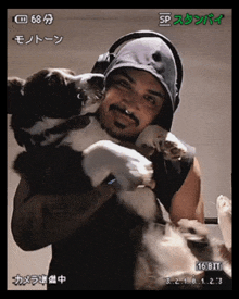 a man is holding a dog in his arms and the time displayed on the screen is 16.8t