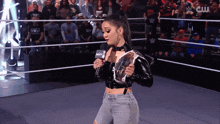 a woman holding a microphone in a wrestling ring with a cw logo on the bottom