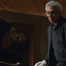 a man with curly hair wearing glasses talks to another man