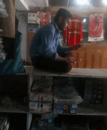 a man sits on a shelf in a store looking at a cell phone