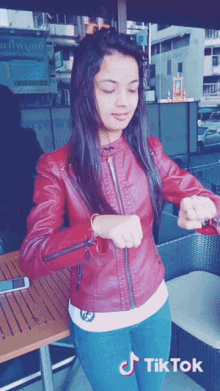 a girl wearing a red leather jacket is looking at her watch with a tiktok logo in the corner