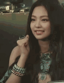 a close up of a woman with long hair wearing a bracelet and a necklace .
