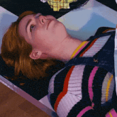 a woman in a striped sweater is laying on her stomach in a coffin .