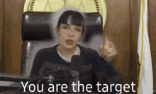 a woman is sitting in a chair in front of a microphone with the words `` you are the target '' .