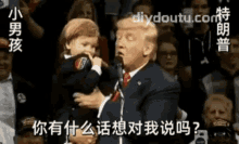 donald trump is holding a baby in his arms while speaking into a microphone in front of a crowd .