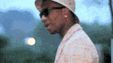 a man wearing a hat and sunglasses is standing in front of a blurry background