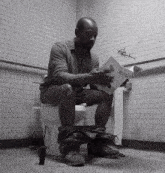 a man is sitting on a toilet reading a book titled " a man 's manual "