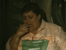 a woman wearing a pink shirt and an apron is eating something