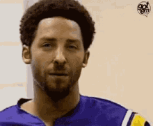 a man with a beard wearing a blue and yellow jersey is making a funny face .