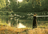 a woman in a black dress is standing on the shore of a lake