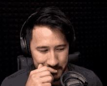 a man wearing headphones is sitting in front of a microphone and covering his mouth .