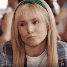 a woman with blonde hair and a green headband is making a face .