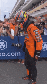 a race car driver stands in front of a blue banner that says ' to.com ' on it
