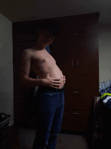 a shirtless man in a hat holds his belly