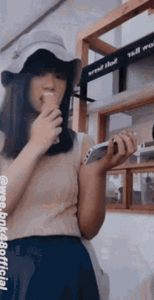 a woman wearing a hat is holding a cell phone and a drink
