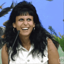a woman is smiling in front of a microphone with a sb logo in the background