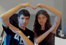 a man and woman make a heart shape with their hands