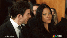 a man and a woman are sitting next to each other with the nbc logo in the background