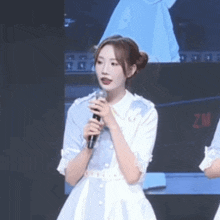 a woman in a white dress is holding a microphone in front of a large screen .