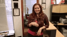 a woman in a leather jacket is standing in front of a desk in an office