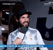 a man with a beard is talking into a microphone while wearing a real madrid shirt .
