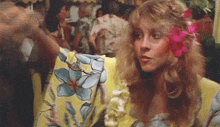 a woman with a flower in her hair is wearing a yellow shirt with a floral pattern .