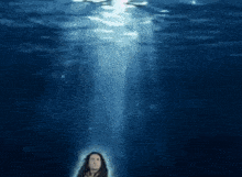 a woman is standing in the water looking up at the light coming out of the water .