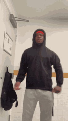 a man wearing a black hoodie and a red headband is standing in a bathroom