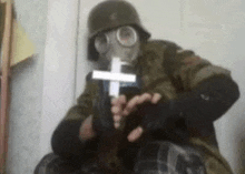 a man in a gas mask is holding a cross in his hand .