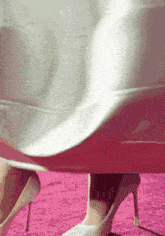 a woman wearing a white dress and high heels is standing on a pink carpet