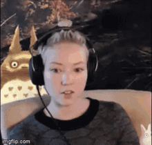 a woman wearing headphones is sitting on a couch with a totoro in the background .