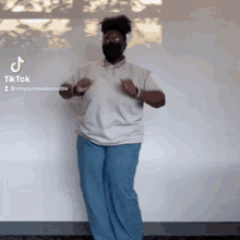 a woman wearing a mask is dancing in front of a wall with tiktok written on the bottom right