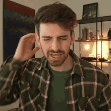 a man with a beard wearing a plaid shirt is scratching his head