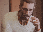 a man wearing glasses and a white sweater holds a small object in his hand