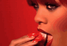a woman with red nails is eating a strawberry with her tongue .