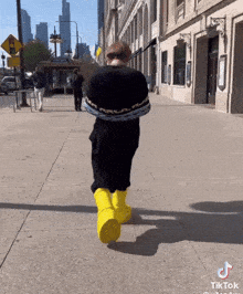 a person wearing a black sweater and yellow boots is walking down a sidewalk with a tiktok logo on the bottom