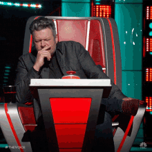 a man sits in a chair with his hand to his mouth and the words #thevoice on the bottom right