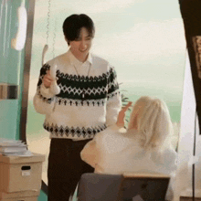 a man and a woman are standing next to each other in a room . the man is wearing a sweater .