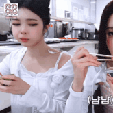 two girls are eating with chopsticks in a kitchen with a sign that says s3