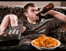 a man sitting on a couch drinking a bottle of beer and eating chips