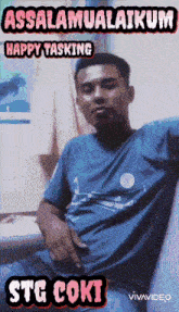 a man in a blue shirt is sitting in front of a sign that says assalamualaikum happy tasking stg coki