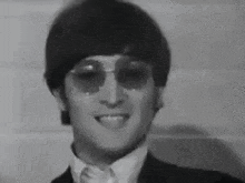 a black and white photo of a man wearing sunglasses and a suit and tie .