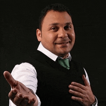 a man wearing a black vest and a green tie is reaching out his hand towards the camera .
