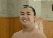 a man with a bun on his head is smiling in front of a sign that says japan sumo