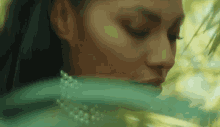 a close up of a woman 's face with green leaves behind her