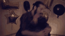 a man is holding another man in his arms at a party with balloons .