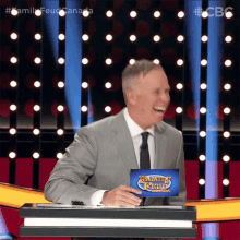 a man in a suit and tie is laughing while holding a family feud sign