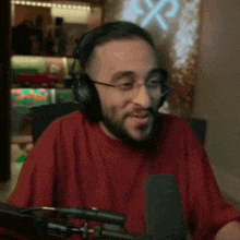 a man wearing headphones and glasses is sitting in front of a microphone in a room .