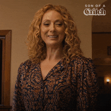 a woman with curly hair is smiling in front of a sign that says son of a bitch