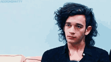 a young man with long black hair is sitting on a couch with his eyes closed .